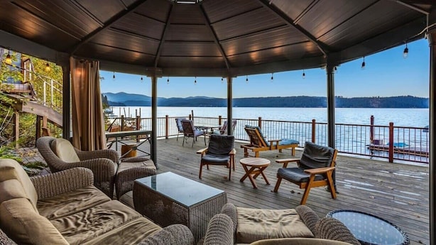 Un espacio de estar techado al aire libre con vistas a un lago y montañas.