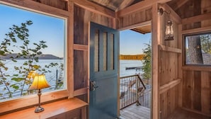 Una cabaña de madera con vista a un lago, una puerta y una lámpara sobre un alféizar de madera.