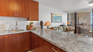 A kitchen with wooden cabinets, a granite countertop, and a dining area with a sofa and chairs. - Relaxing Oceanfront! (Wailuku)