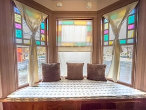 A bay window with three cushions, a patterned pillow, and a view of the outside.