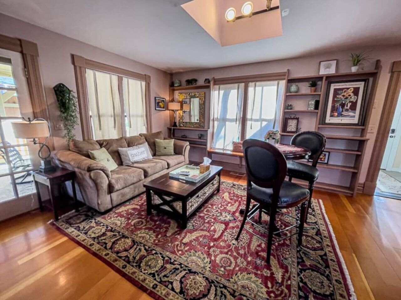 A living room with a sofa, coffee table, and chairs, a rug, and a bookshelf with framed pictures.
