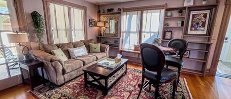 A living room with a sofa, coffee table, and chairs, a rug, and a bookshelf with framed pictures.