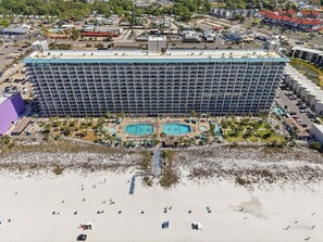 A large hotel with multiple floors, a central pool area, and a beach in the foreground.