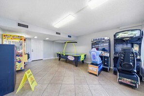 A room with a pool table, arcade machines, and a toy chest.
