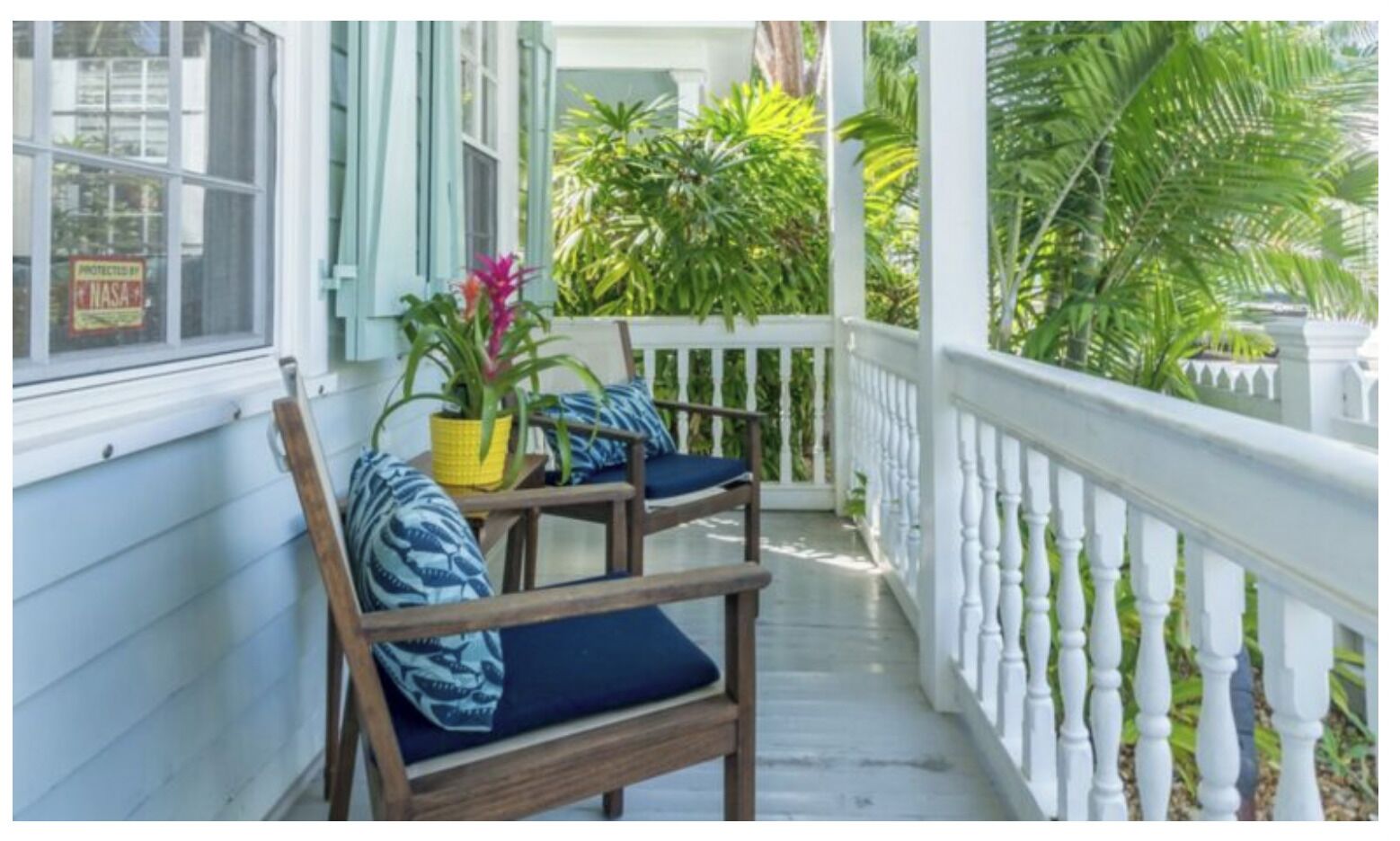 A porch with two wooden chairs, a potted plant, and a white railing.