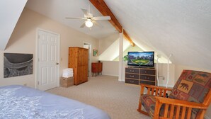 Ein Schlafzimmer mit einem Bett, einem Holzstuhl, einem Fernseher, einem Kleiderschrank und einem Deckenventilator.