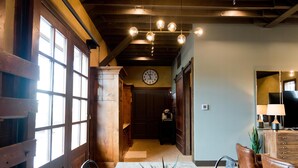 A dining area with a wooden table, chairs, and a potted plant. There is a clock on the wall and a chandelier above. - Depot Flat - Kitchenette, 2 Queen Murphy Beds, Large Sitting Area (Logan)