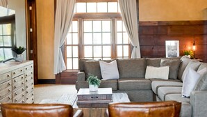 A cozy living room with a sectional sofa, a wooden coffee table, and a large window with curtains. - Depot Flat - Kitchenette, 2 Queen Murphy Beds, Large Sitting Area (Logan)