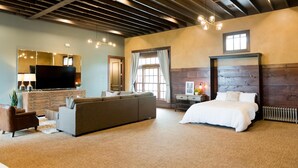 A spacious bedroom with a large bed, a sofa, a TV, and a dresser. - Depot Flat - Kitchenette, 2 Queen Murphy Beds, Large Sitting Area (Logan)