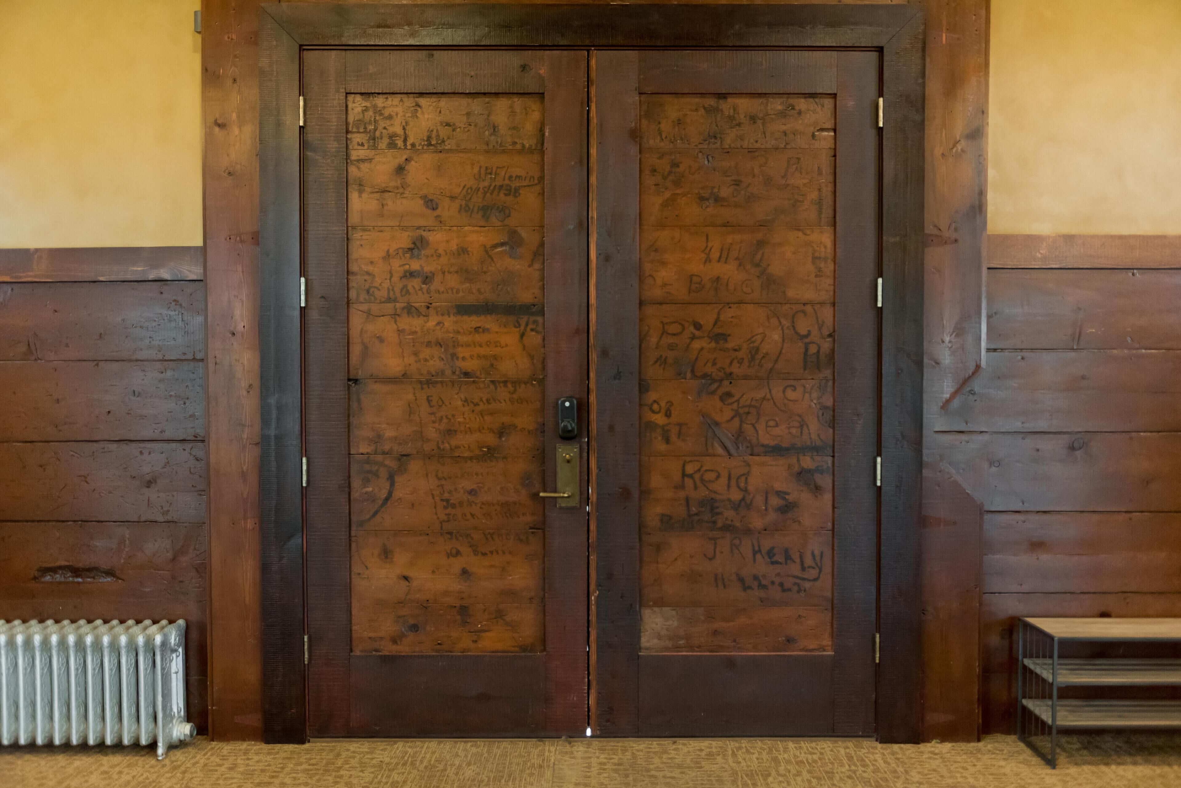 A wooden double door with various writings and a metal handle.