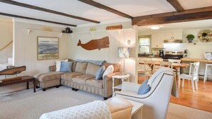A cozy living room with a sofa, armchair, and a dining area with a table and chairs. - Great Home with Game Space, 0.8 miles from Cooks Brook Beach! (Eastham)