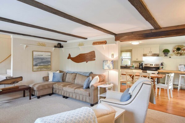 A cozy living room with a sofa, armchair, and a dining area with a table and chairs. - Great Home with Game Space, 0.8 miles from Cooks Brook Beach! (Eastham)