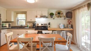 A kitchen with white cabinets, a wooden table, and white chairs. - Great Home with Game Space, 0.8 miles from Cooks Brook Beach! (Eastham)