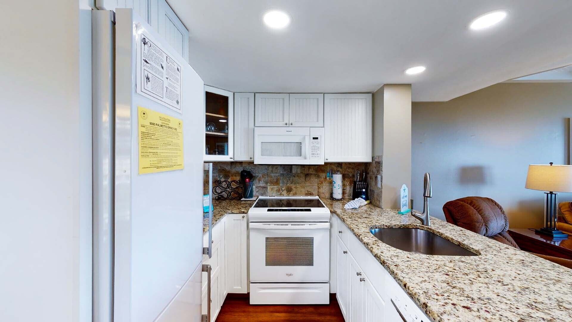 A modern kitchen with white cabinets, a granite countertop, a built-in microwave, and a stainless steel sink.
