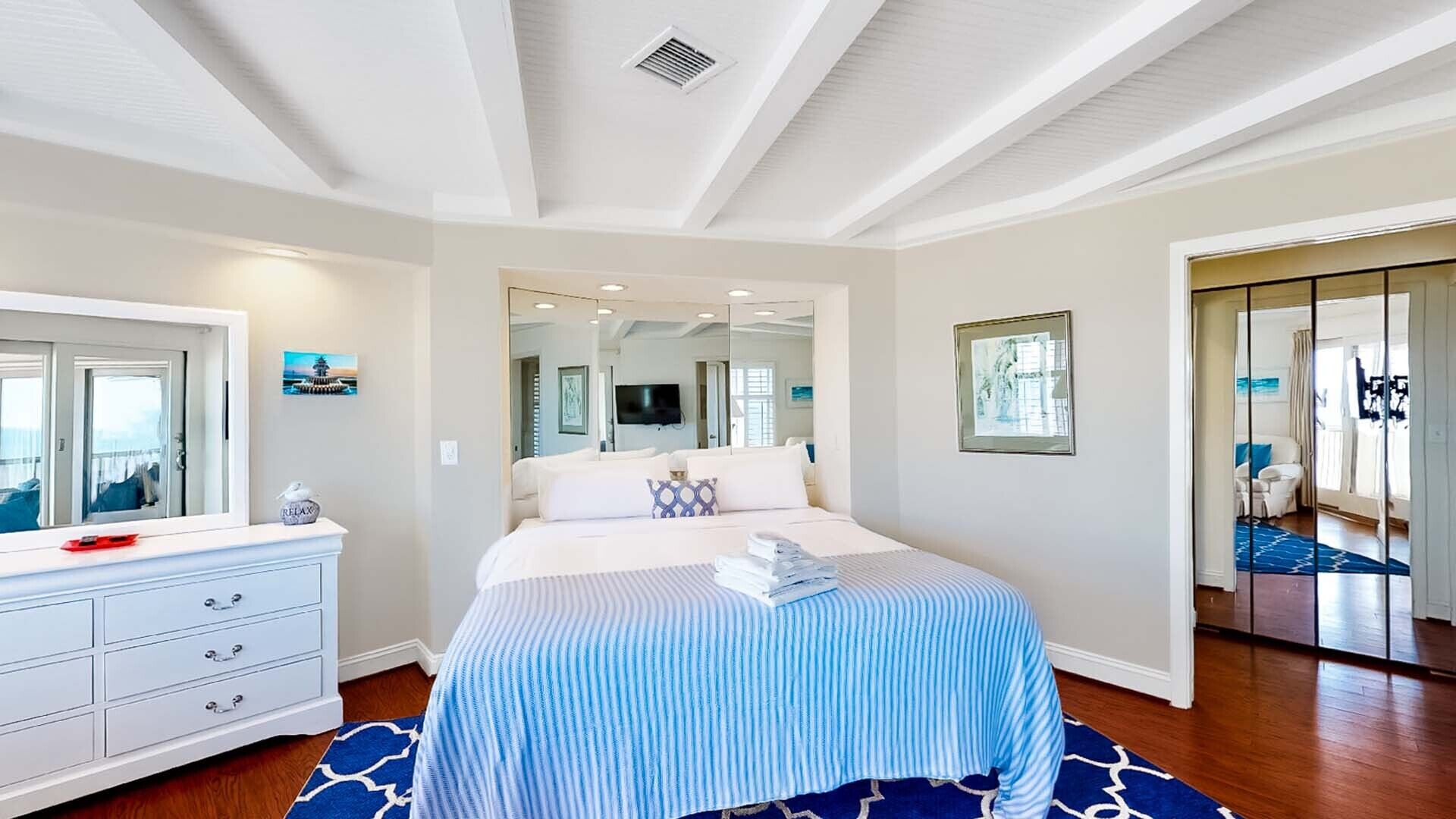 A bedroom with a large bed, a dresser, a mirror, and a view of the living area.