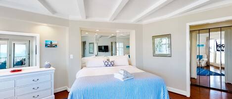 A bedroom with a large bed, a dresser, a mirror, and a view of the living area.