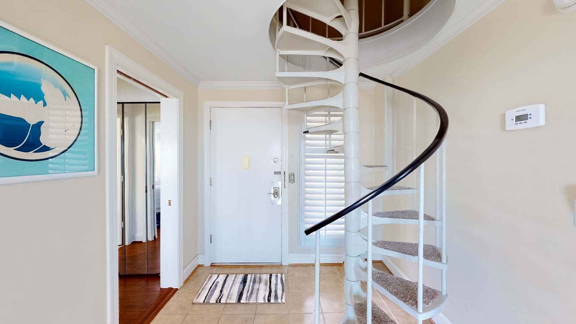 Una escalera de caracol con detalles blancos y barandal negro, que conduce a una plataforma con una puerta y un ventanal con persianas.