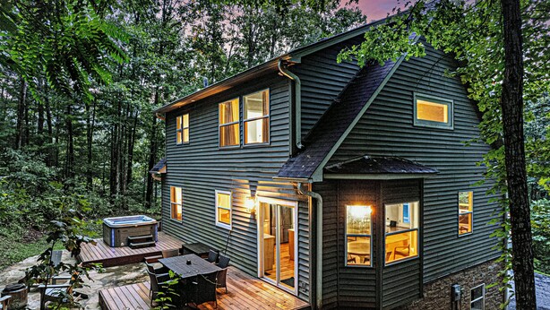 A two-story cabin with a deck, outdoor seating, and a hot tub.