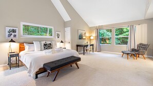 A bedroom with a large bed, a desk, a chair, and a window with curtains.