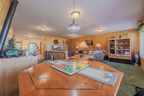 A cozy room with a wooden interior, a dining table with board games, a fireplace, and a bookshelf.