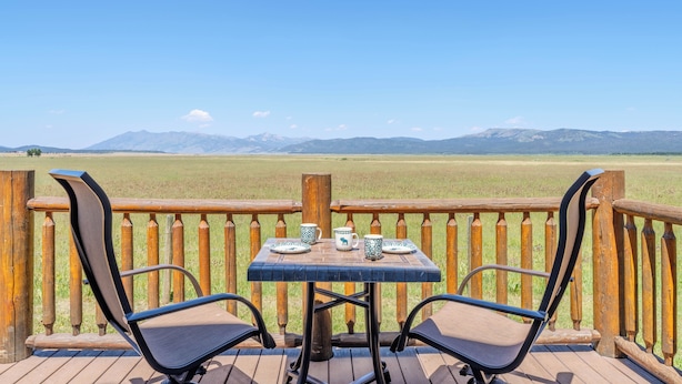 Una terraza con una mesa y sillas que da a un campo césped y montañas.
