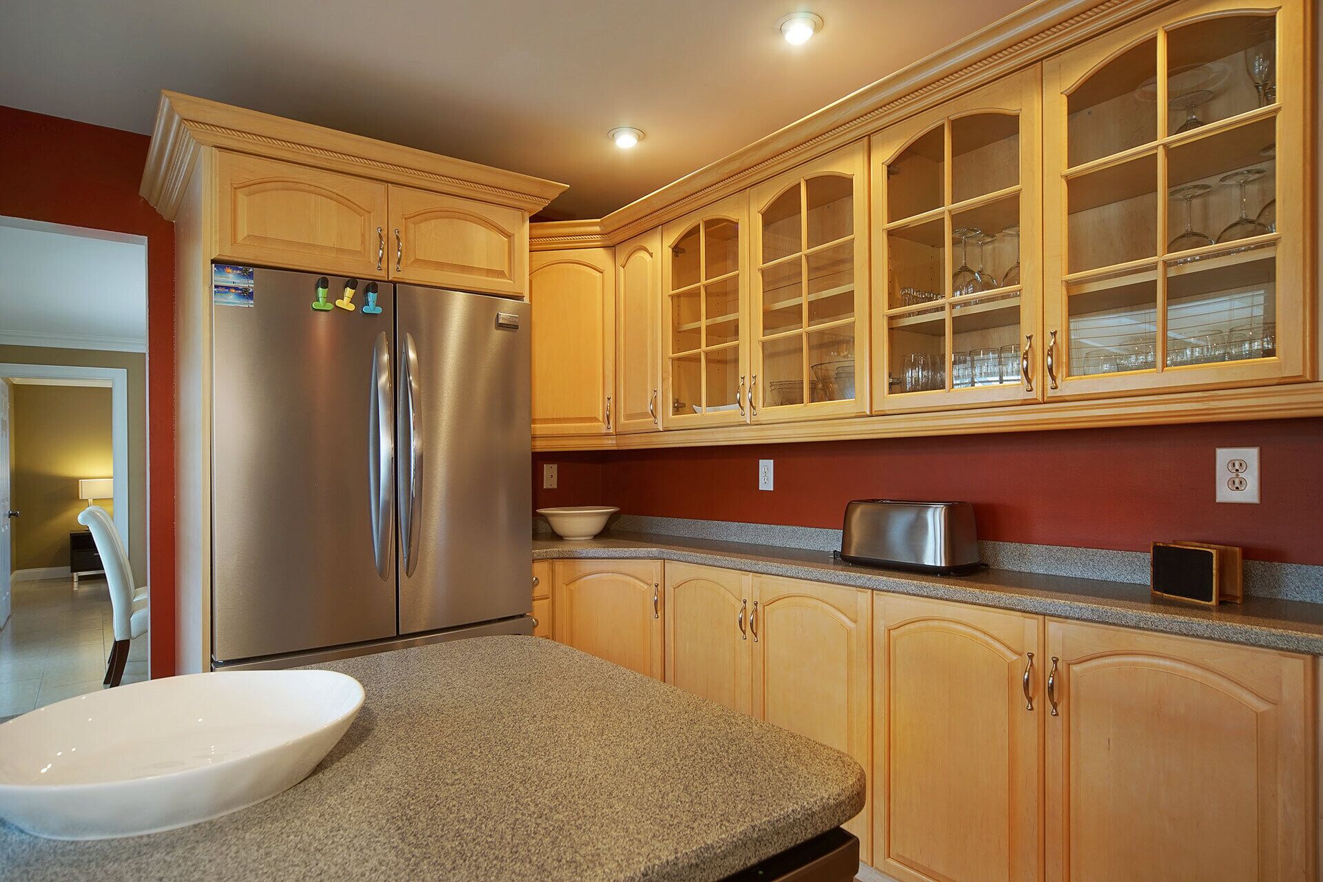 A kitchen with wooden cabinets, a stainless steel refrigerator, a granite countertop, and a toaster.