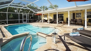 Zona de piscina con cerramiento de cristal, sillas de descanso y comedor.