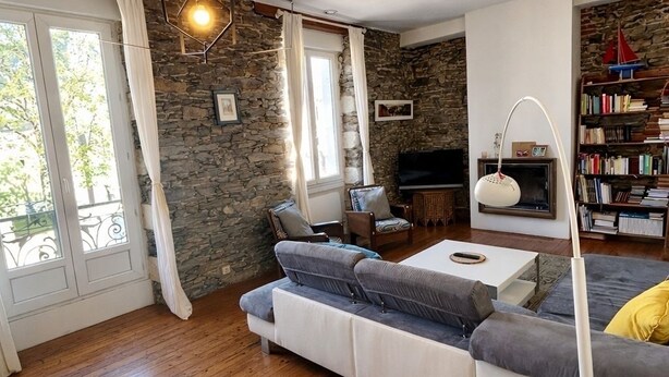 A living room with a stone wall, wooden flooring, a sofa, a TV, a bookshelf, and a ceiling light fixture. - Namaste Duplex Gare Nantes  (Nantes)