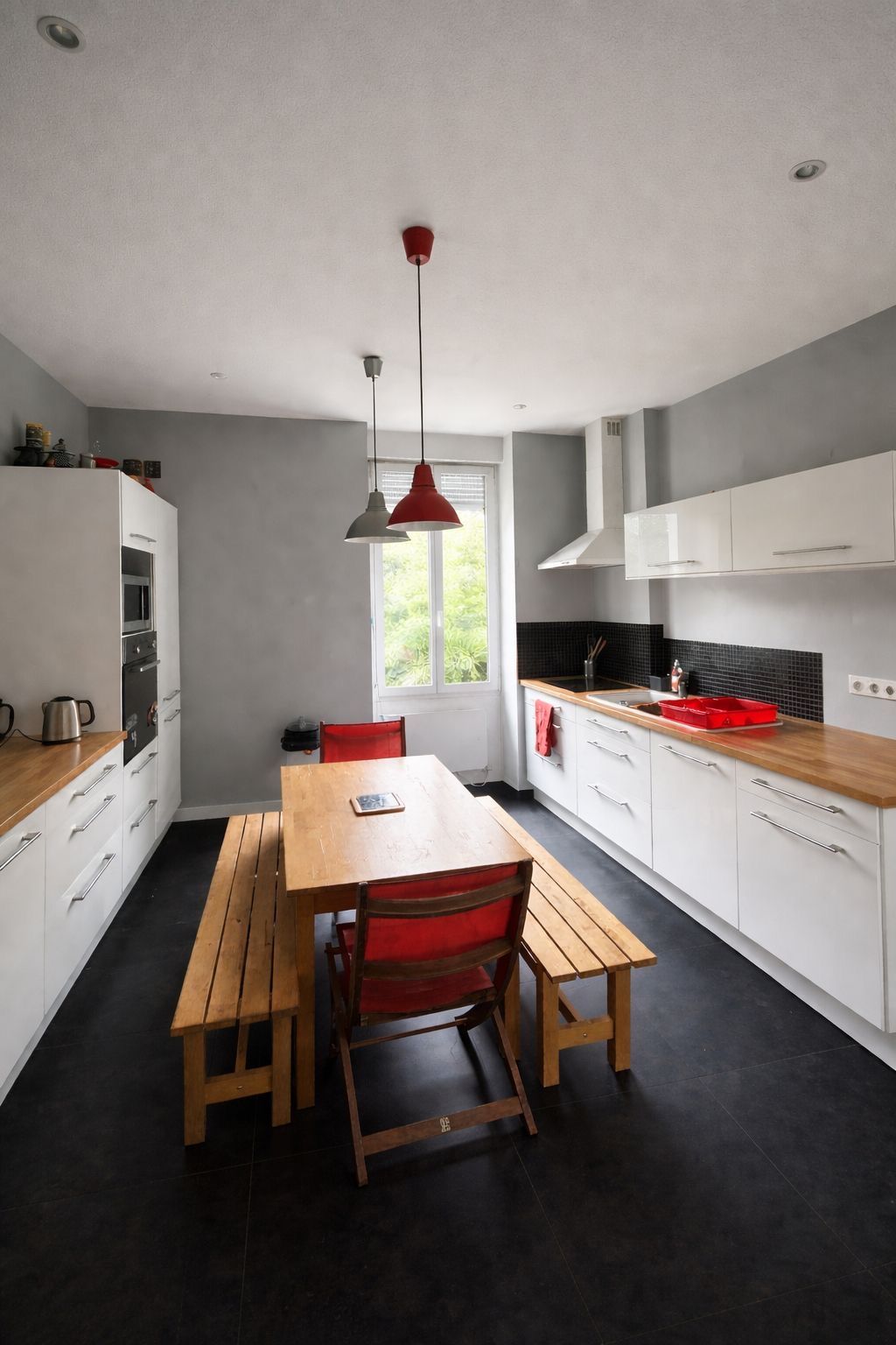 A modern kitchen with white cabinets, a wooden table, and red chairs.