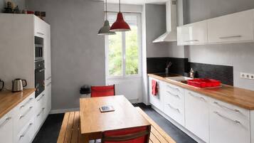 A modern kitchen with white cabinets, a wooden table, and red chairs.