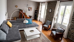 A living room with a grey sofa, a white coffee table, a patterned rug, a wooden chair, and a stone wall. - Namaste Duplex Gare Nantes  (Nantes)