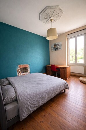 A bedroom with a bed, a desk, a chair, a window, and a ceiling light fixture.