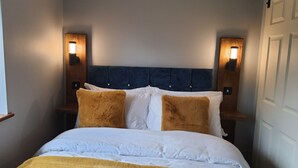 Een bed met wit- en bruin beddengoed, een blauw hoofdbord en twee wandlampen aan weerszijden.