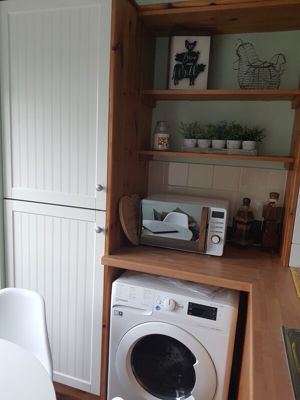 Un espacio de lavandería pequeño con lavadora, un tendedero y un estante con objetos decorativos.