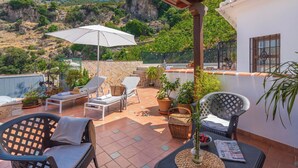 A rooftop terrace with lounge chairs, a table, and potted plants.