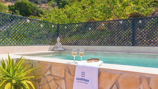 A pool area with a stone wall, a white towel with a logo, and two glasses of white wine.