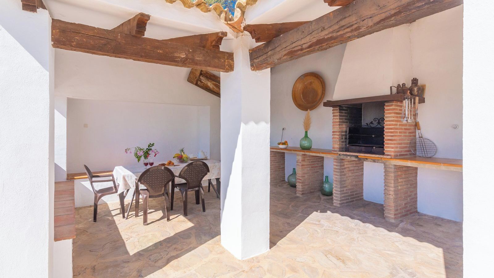 An outdoor patio with a brick barbecue, stone flooring, and a table set for dining.