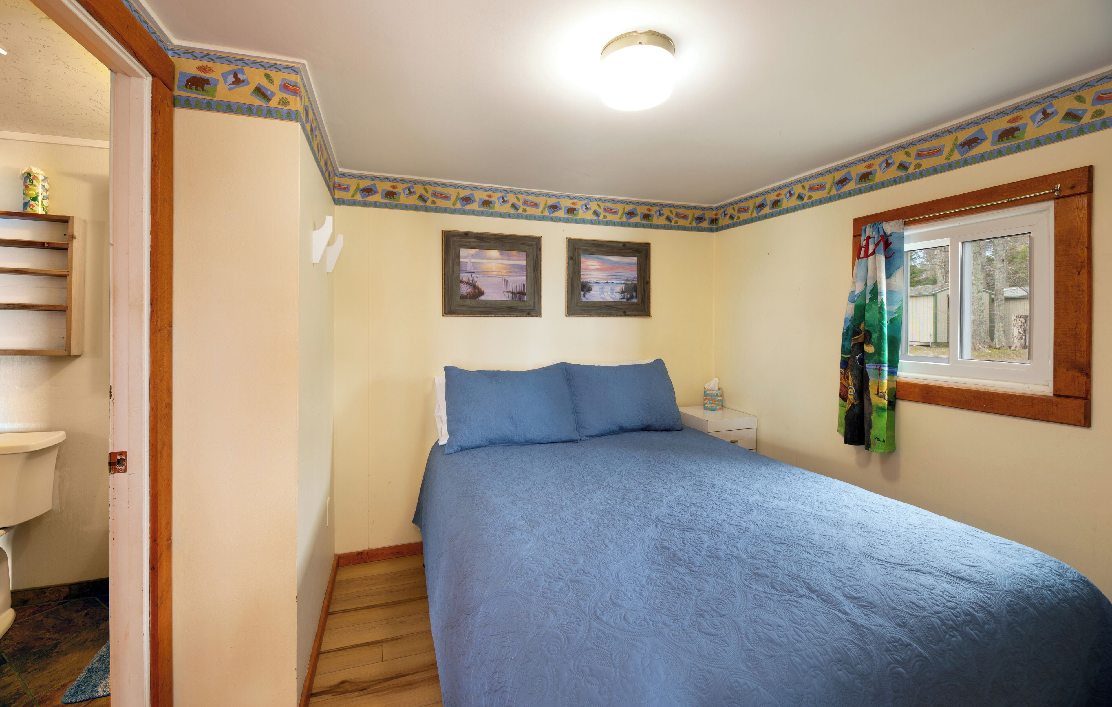 A bedroom with a bed, a window with a curtain, and two framed pictures on the wall.