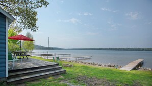 A lakeside deck with a picnic table and chairs, a red umbrella, and a dock extending into the water. - Waters Edge Lakefront Cottage between Glen Arbor & Leland (Maple City)