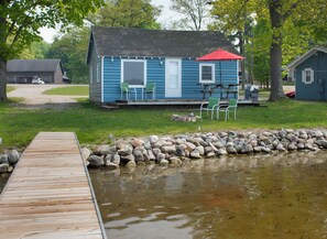 A cabin with a dock leading to a pond, surrounded by a grassy area and trees. - Waters Edge Lakefront Cottage between Glen Arbor & Leland (Maple City)