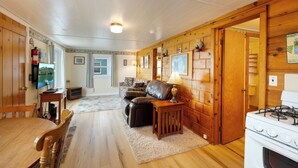 A cozy cabin interior with a dining area, a sofa, a fireplace, and a kitchen with a stove. - Waters Edge Lakefront Cottage between Glen Arbor & Leland (Maple City)