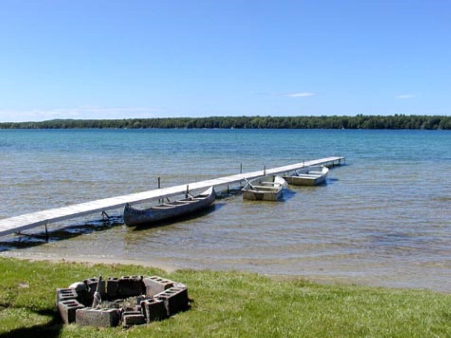 A dock with boats and a grassy area with a fire pit.