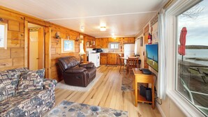 A cabin interior with a living area, kitchen, and a large window overlooking a body of water. - Waters Edge Lakefront Cottage between Glen Arbor & Leland (Maple City)