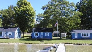 A dock with boats, a small blue building, and a flagpole with an American flag. - Waters Edge Lakefront Cottage between Glen Arbor & Leland (Maple City)