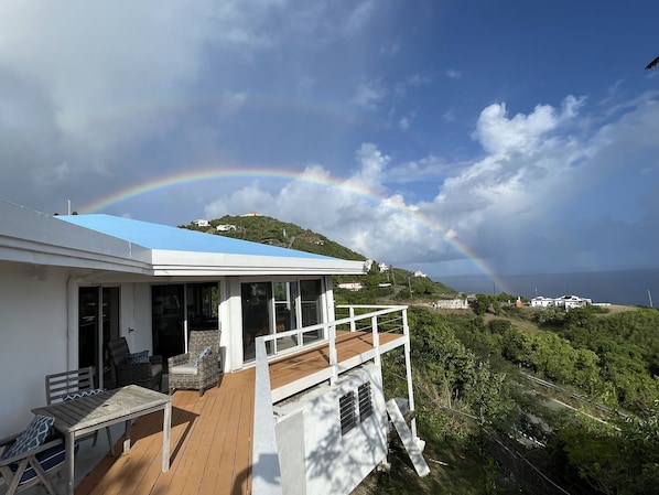 A house with a blue roof, a wooden deck, and a view of a hill with houses and a rainbow. - Ultimate USVI Views overlooking Caribbean & Salt River Bay Nat'l EcoPreserve (Christiansted)