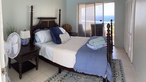 A bedroom with a four-poster bed, a nightstand with a lamp, a large window with a view of the sea, and a sliding door leading to a balcony. - Ultimate USVI Views overlooking Caribbean & Salt River Bay Nat'l EcoPreserve (Christiansted)