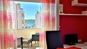A room with a balcony, a TV, a desk, and a red accent wall.