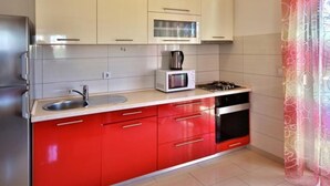A kitchen with white upper cabinets, a red lower cabinet, a microwave, a gas stove, and a stainless steel sink.