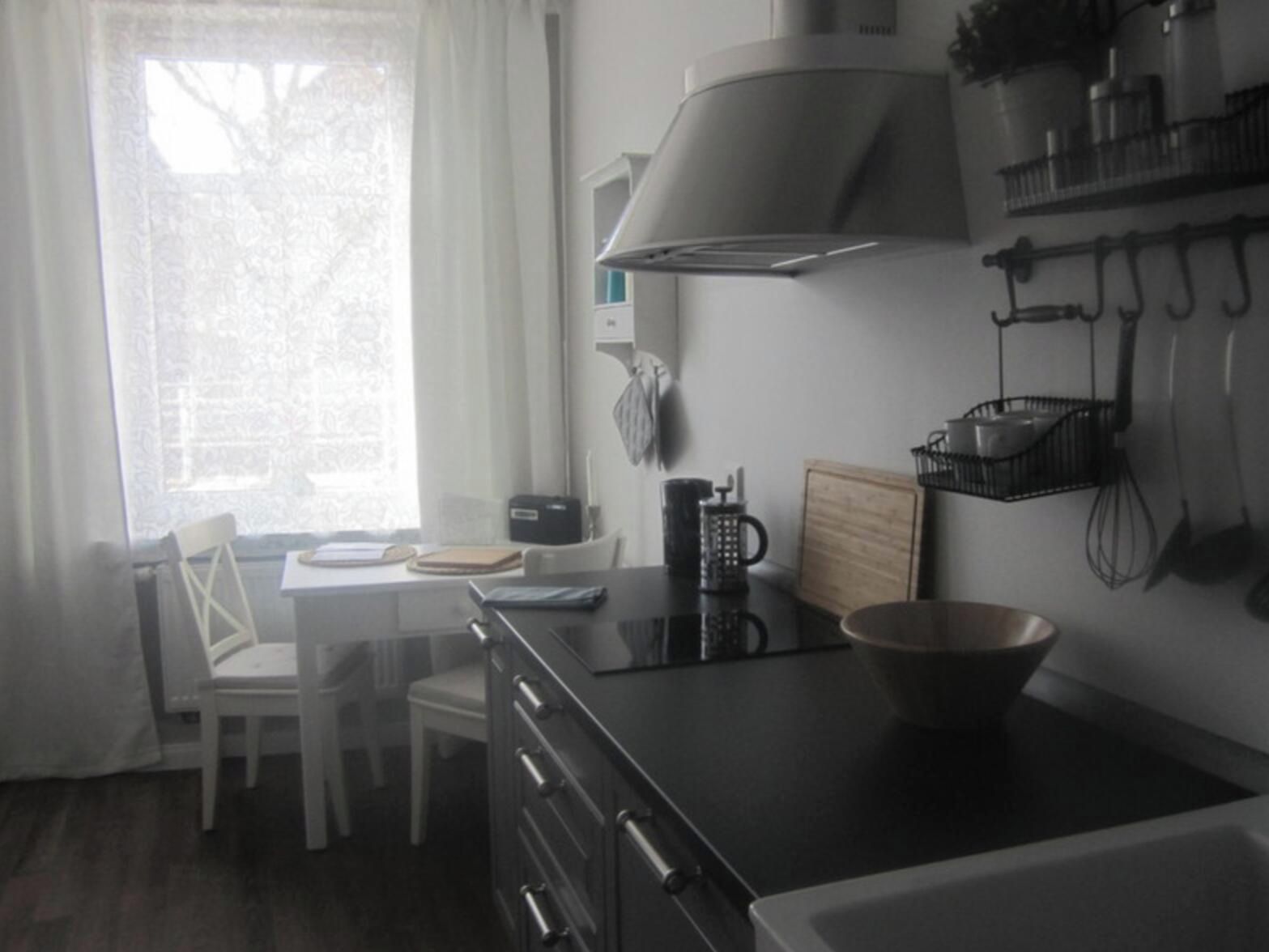 Uma cozinha com fogão, pia, janela com cortinas e uma cadeira.