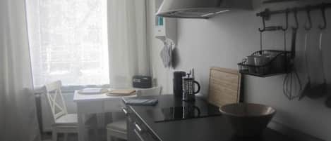 A kitchen with a stove, a sink, a window with curtains, and a chair.